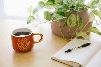 inspirational coffee mug and notebook on table / internal clock
